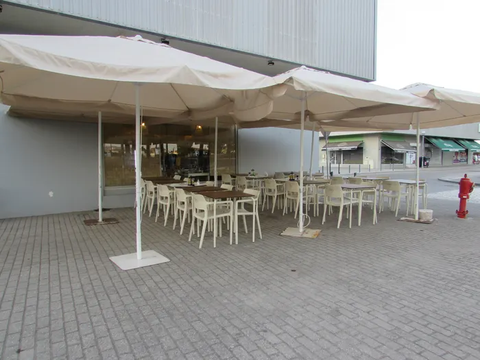 Esplanada com mesas e cadeiras brancas debaixo de guarda-sóis, à porta do restaurante