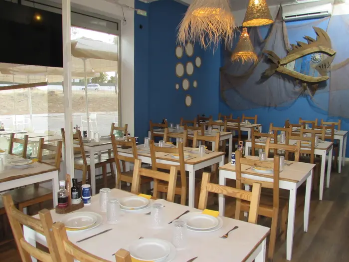 Sala com parede azul, peixe de madeira e redes de pesca, candeeiros de palha e mesas postas
